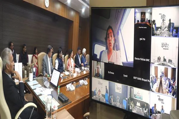 सम्मेलन कक्ष में अधिकारी और बड़ी स्क्रीन पर वीडियो कॉन्फ्रेंस से जुड़े जिलों के अधिकारी